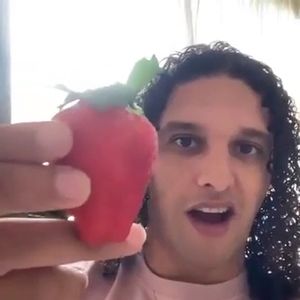 Ali B die een bovengemiddelde aardbei naast zijn hoofd houdt